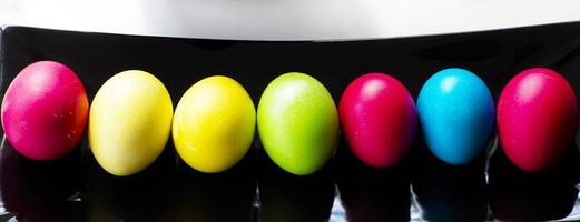 Pasqua multicolore uova nel un' riga su un' nero rettangolare piatto. foto