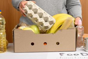 donna nel guanti mantiene raccolta cibo, frutta e cose e un' cartone scatola per porzione quelli nel bisogno foto