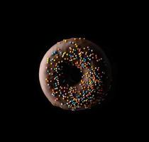 cioccolato ciambelle con multicolore spruzzatori levitare su un' nero sfondo foto