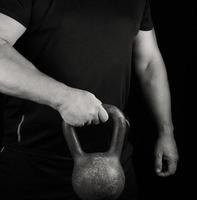 adulto forte atleta nel nero Abiti Tenere un ferro kettlebell su il suo braccia foto