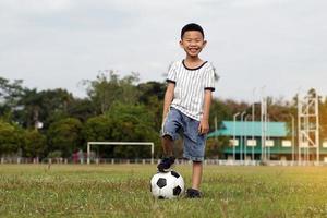 asiatico ragazzo passo su un' palla mentre calciando calcio su il campo. morbido e selettivo messa a fuoco. foto
