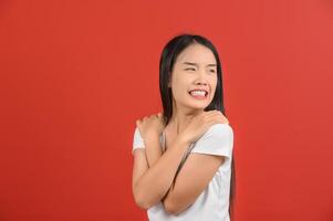 ritratto di giovane asiatico donna nel bianca maglietta abbracciare se stessi contento e positivo isolato su rosso sfondo foto