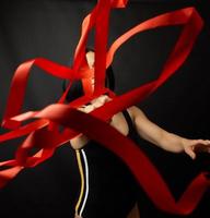 giovane donna ginnasta di caucasico aspetto con nero capelli gira rosso raso nastri foto