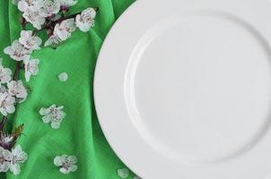 vuoto bianca piatto su un' verde tovagliolo con ciliegia fiori foto