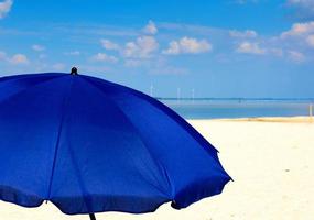 tessile blu ombrello su il sfondo di il mare e cielo con bianca nuvole foto