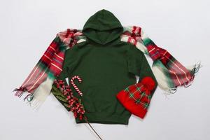 vicino su verde vuoto modello felpa con cappuccio copia spazio. Natale vacanza concetto. superiore Visualizza modello felpa, sciarpa, cappello. rosso vacanze decorazioni bianca sfondo. contento nuovo anno Accessori. selettivo messa a fuoco foto