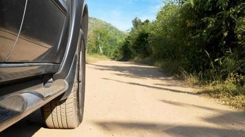 pneumatici di un' grigio auto in viaggio e passo su il sporco strada. sporco strada con alberi e erba su tutti e due lati sotto blu cielo. foto