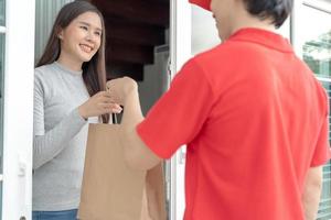 contento sorridente asiatico donna riceve carta Borsa pacco di cibo a partire dal Corriere davanti Casa. consegna uomo Spedire consegnare esprimere. in linea acquisti, carta contenitore, porta via, postino, consegna servizio, pacchi foto