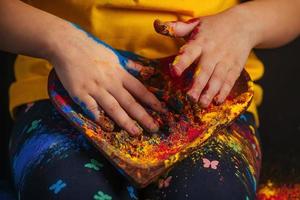 figli di mani hold un' di legno piatto nel il forma di un' cuore nel quale il multicolore luminosa colori di holi. indiano Festival di colori holi. foto