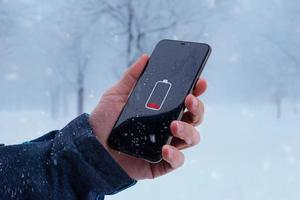 Basso batteria su smartphone nel uomo mano. inverno, freddo volta. concetto di Più veloce batteria scarico a Basso temperature foto