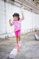 bambina asiatica che cammina sul marciapiede e cerca di mantenere l'equilibrio foto