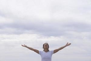 donna di fronte con la camicia bianca alzando le braccia al cielo foto