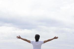 donna in maglietta bianca alzando le braccia di fronte al mare foto