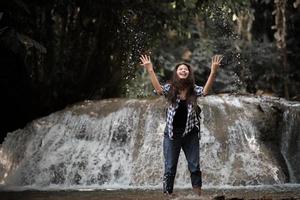 giovane donna che ha divertimento sotto una cascata nella foresta foto