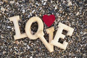 lettere di legno che formano la parola amore con un cuore rosso su uno sfondo di spiaggia di sabbia. concetto di san valentino foto