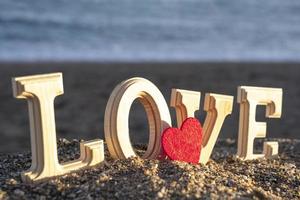 lettere di legno che formano la parola amore con un cuore rosso in riva al mare. concetto di amanti foto