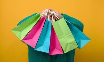 un' donna nel un' maglione detiene un' carta Borsa su un' giallo sfondo e Spettacoli un' piace gesto con sua mano. acquisti. di stagione vendita foto