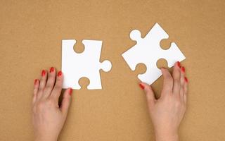 Due vuoto carta bianca pezzi di puzzle nel femmina mani, puzzle collegato, Marrone sfondo foto