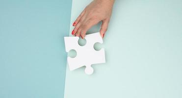 femmina mano detiene un' frammento di un' bianca grande puzzle su un' blu sfondo foto