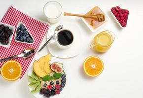 tazza di nero caffè, un' piatto di fiocchi d'avena e frutta, miele e un' bicchiere di latte su un' bianca tavolo, salutare mattina colazione, superiore Visualizza foto