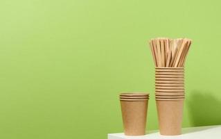 Marrone carta cartone tazze e di legno eccitante bastoni su un' bianca tavolo, verde sfondo. eco-friendly vasellame foto