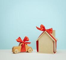 modello di un' di legno Casa e auto giocattolo legato con un' rosso seta nastro su un' blu sfondo, concetto di vero tenuta Acquista, mutuo foto