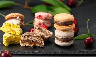 pila di multicolore macarons e maturo rosso ciliegie su nero di legno sfondo foto