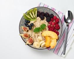 bollito fiocchi d'avena con frutta nel un' il giro piatto su un' bianca tavolo, salutare prima colazione foto