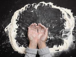 setacciato bianca Grano Farina su un' nero tavolo e Due femmina mani, superiore Visualizza. cucinando a casa foto