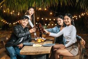 ritratto di contento asiatico amici avendo cena festa insieme - giovane persone seduta a bar tavolo tostatura birra bicchieri cena all'aperto - le persone, cibo, bevanda stile di vita, nuovo anno celebrazione concetto. foto