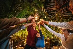ritratto di contento asiatico gruppo di amici avendo divertimento con sparklers all'aperto - giovane persone avendo divertimento con fuochi d'artificio a notte tempo - le persone, cibo, bevanda stile di vita, nuovo anno celebrazione concetto. foto