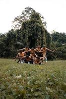 un' gruppo di indonesiano persone danza posa nel un' d'oro completo da uomo mentre indossare trucco su il verde erba foto