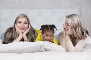 famiglia a partire dal diverso gare. mamma nonna di carnagione chiara e un' poco africano americano ragazza menzogna su il divano. foto