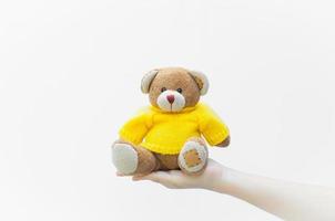 donna Tenere e proteggere dare un' Marrone orsacchiotto orso giocattolo indossare giallo camicie seduta su bianca sfondo primo piano, simbolo di amore o incontri foto