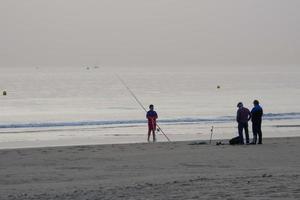 solitario spiaggia con persone passeggiando su il sabbia a il bordo di il mare onde foto