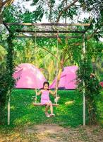 bambina in un abito rosa seduto su un'altalena durante il campeggio foto