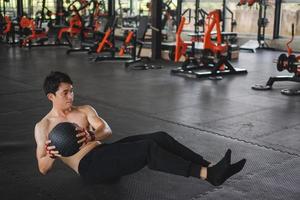 muscolare uomo esercizio con un' pilates palla a il palestra. maschio seduta su il pavimento e fare un' allenarsi utilizzando un' medicina sfera. foto