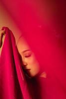 un' bellissimo balinese donna coperto sua trucco viso con rosso tessuto a partire dal il vestito foto