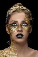 avvicinamento ritratto di bellissimo giovane donna con d'oro Foglio su viso. creativo d'oro trucco su nero sfondo foto