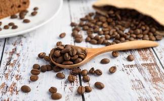 chicchi di caffè in un cucchiaio di legno e sacchi di canapa su un tavolo di legno bianco foto