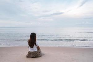 solitario giovane asiatico donna seduta su il spiaggia a tramonto foto