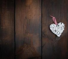bianca di vimini cuore su un' Marrone di legno tavola sfondo foto