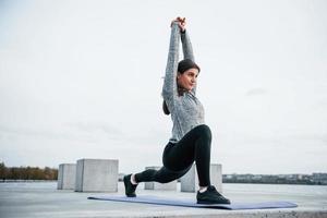 giovane allegro ragazza fare yoga esercizi su fitness stuoia all'aperto vicino lago a giorno foto