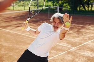 giocando gioco. anziano moderno elegante uomo con racchetta all'aperto su tennis Tribunale a giorno foto