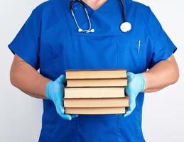 medico nel blu uniforme e sterile latice guanti detiene un' pila di libri nel il suo mano foto