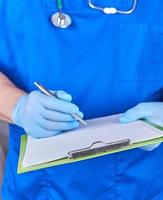 medico nel blu uniforme detiene un' penna e carta titolare foto