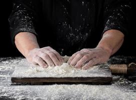 cucinare nel un' nero uniforme mettere Due mani su un' tavolo foto