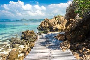 isola tropicale rock e ponte di legno sulla spiaggia con cielo blu nuvoloso foto