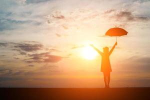 silhouette di una donna con un ombrellone sulla spiaggia e al tramonto foto