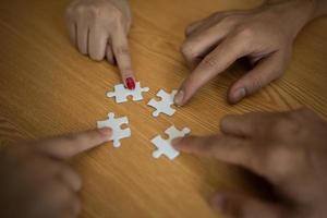 mani che collegano il pezzo di puzzle insieme sulla tavola di legno foto